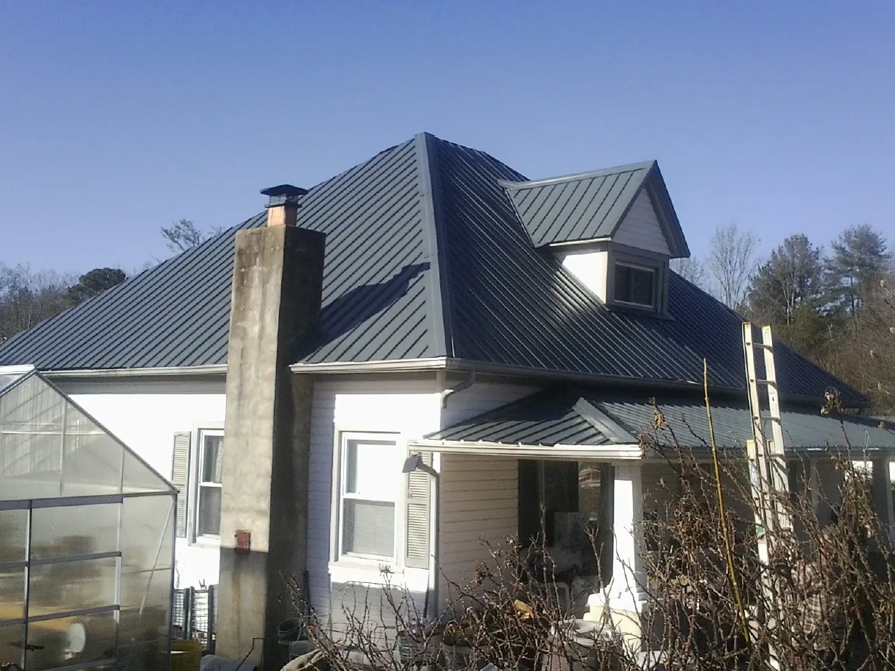 Dark blue standing seam metal roof on a white farmhouse with dormer — Slate & Tile Roof Repair by Roofing Brothers in Brandon